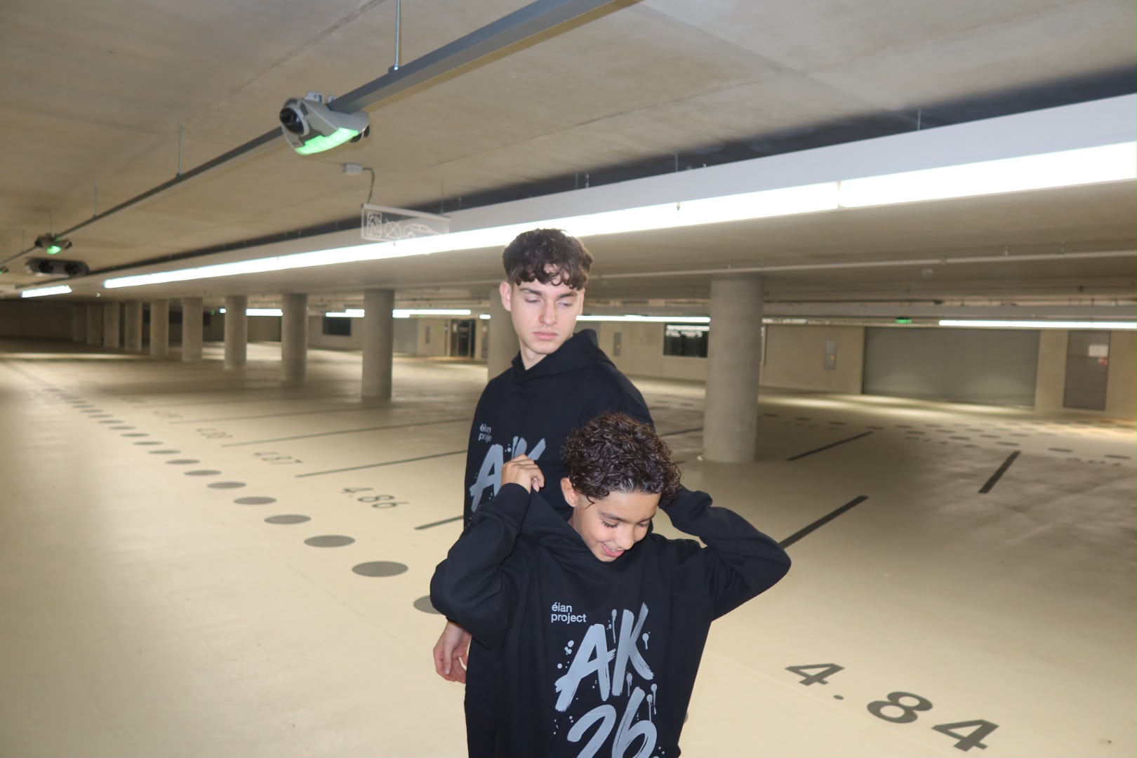Zwei Jungs in schwarzen AK 26 Hoodies in einer leeren Tiefgarage